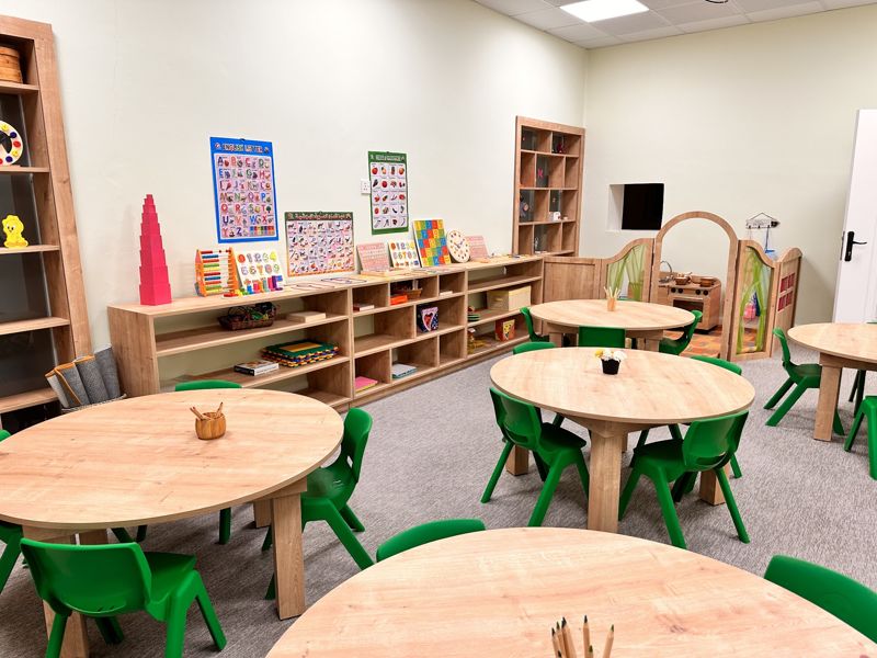 Montessori classroom with small tables, chairs and material shelves